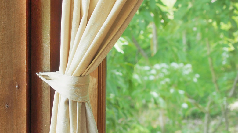 Beige curtains tied back over window overlooking trees