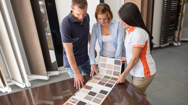 A couple look at flooring swatches with a sales clerk in a showroom.