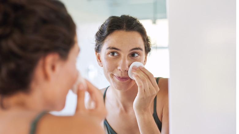 a person looking at their reflection touches a cotton round to their face