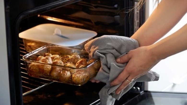 Person loading a glass food storage container into the oven