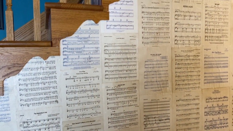 Pages of sheet music are used as wallpaper on a wall under a stairwell.