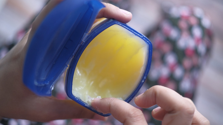 Person scoops out some petroleum jelly out of a plastic tub.