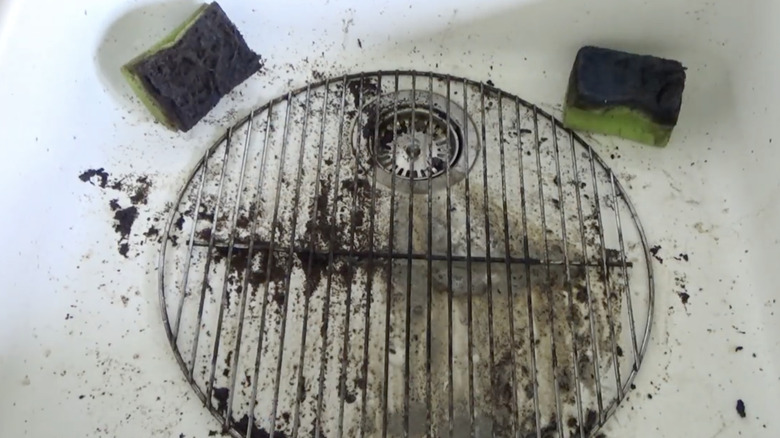 A dirty grill grate in a sink being cleaned with coffee and sponges