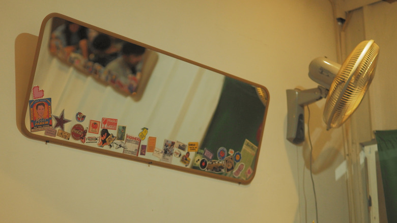 Stickers on a mirror mounted to a bedroom wall next to a fan.
