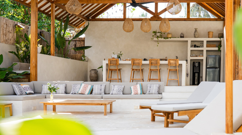 Bohemian patio design with rattan bar stools and bar, L-shaped sofa, and upholstered loungers