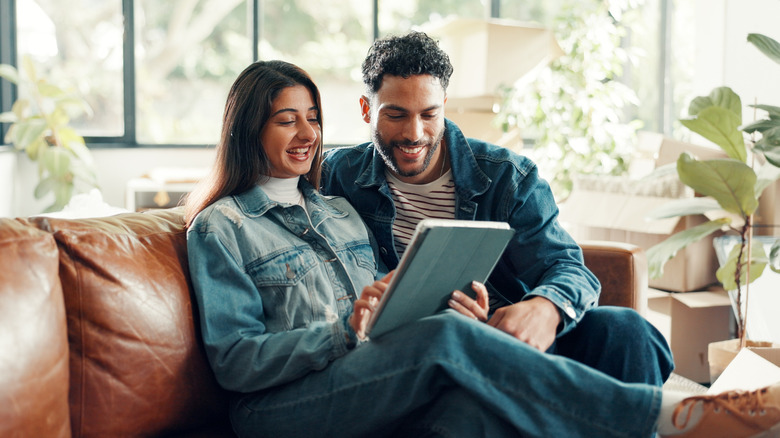 Couple sitting on couch together and looking at tablet to shop for furniture online