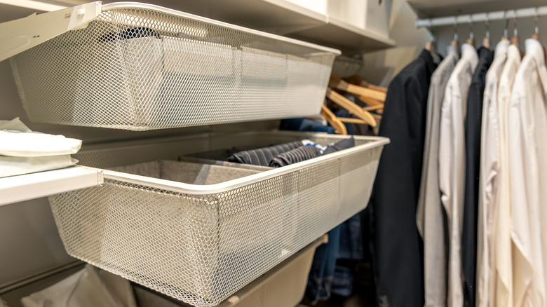 Mesh wire basket installed inside a closet, holding clothing garments.