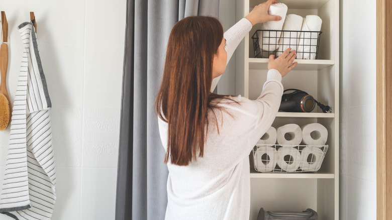 Woman putting a metal basket with towels in it on a shelf in the bathroom