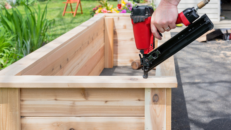 A person building a timber raised garden bed with a drill in hand