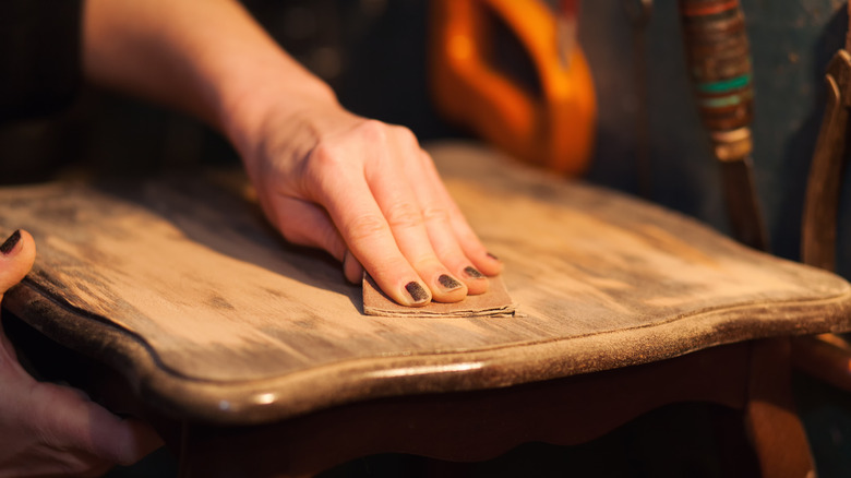 A hand sanding a piece of wood furniture