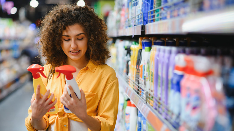 Woman holding two bottles of cleaning spray at the store to choose between products