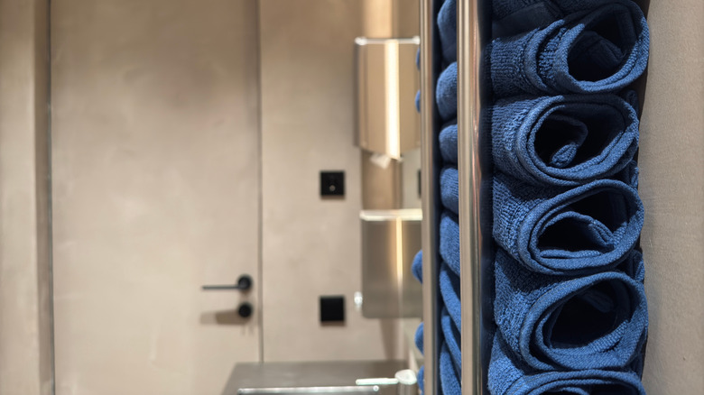 A set of blue towels are rolled up and stacked vertically against the wall of a bathroom.