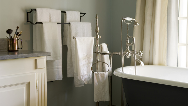 A set of towels on racks behind a standing bathtub.