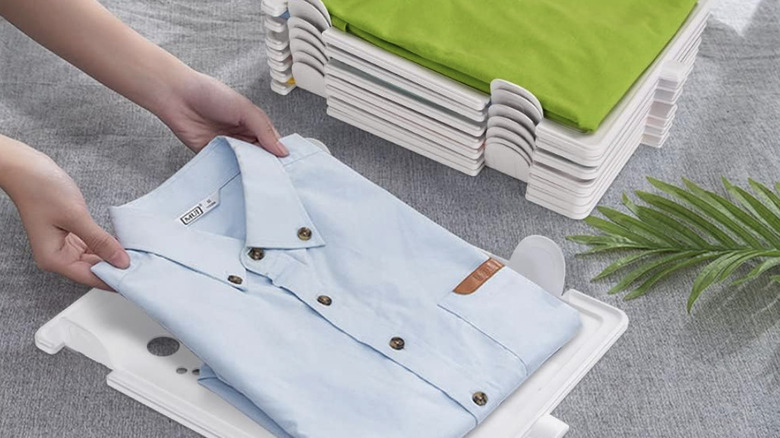 A person lays a folded shirt on a stackable plastic organizer next to a stack of other organizers with shirts