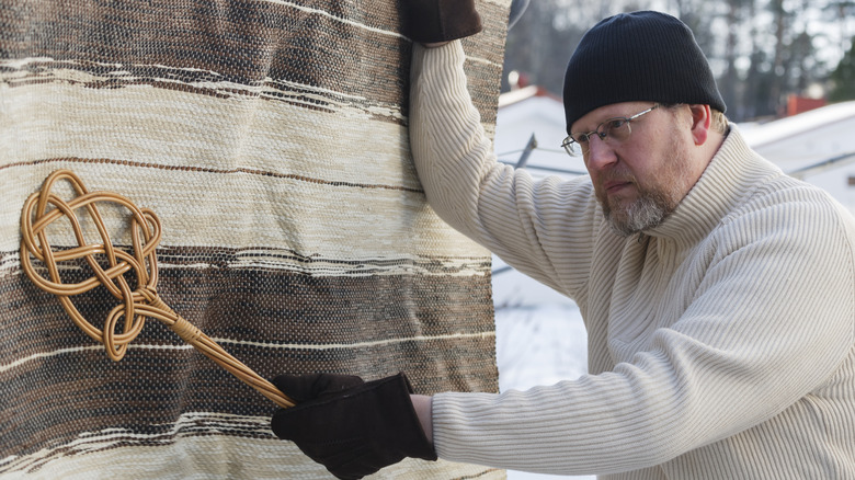 A man using a carpet beater to hit a rug draped on a clothes line