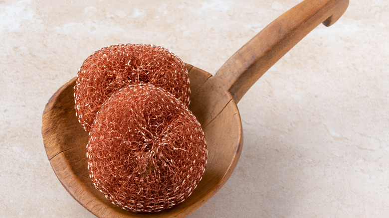 Two copper scrubbing pads in a wooden bowl