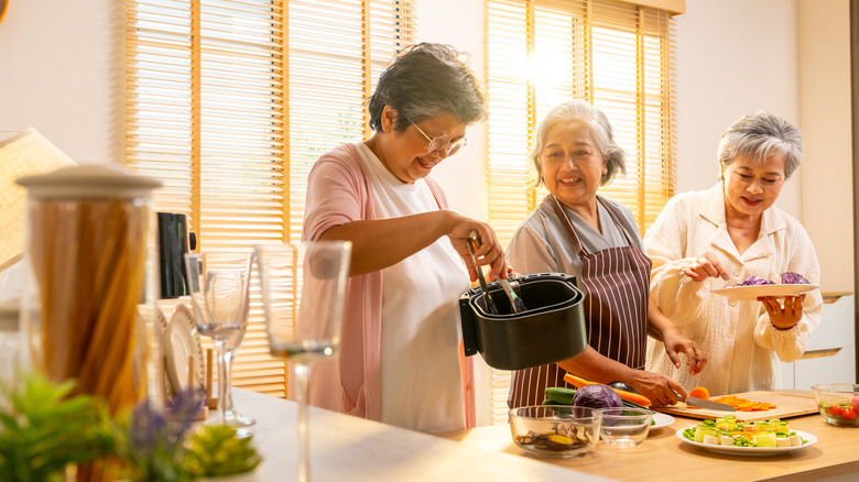 Three senior women cooking together in a sunny kitchen