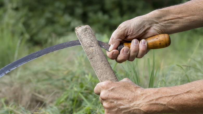 Close-up of hands sharpening the blade of a sickle