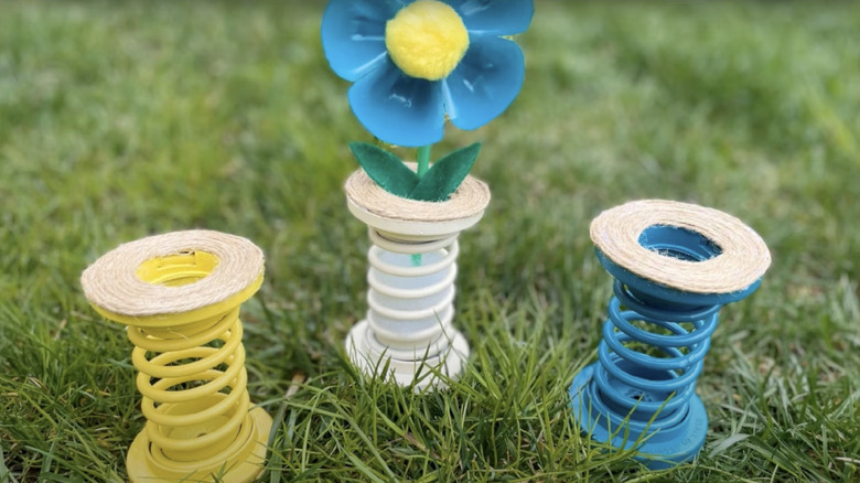 Yellow, blue, and white vases for imitation flowers made from spray painted tension springs and twine.