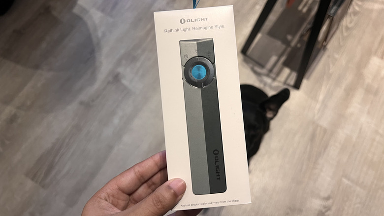 Hand holding the Olight ArkPro in its box above an apartment floor