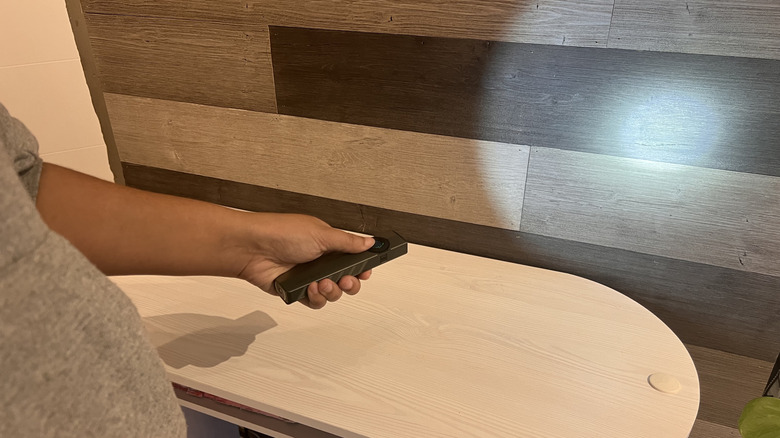 Person pointing Olight ArkPro at a wood paneled wall