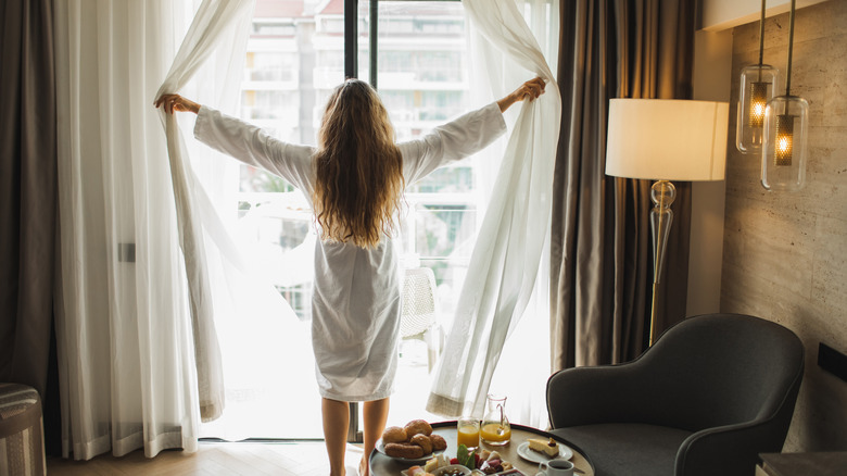 Woman opening curtains of large window