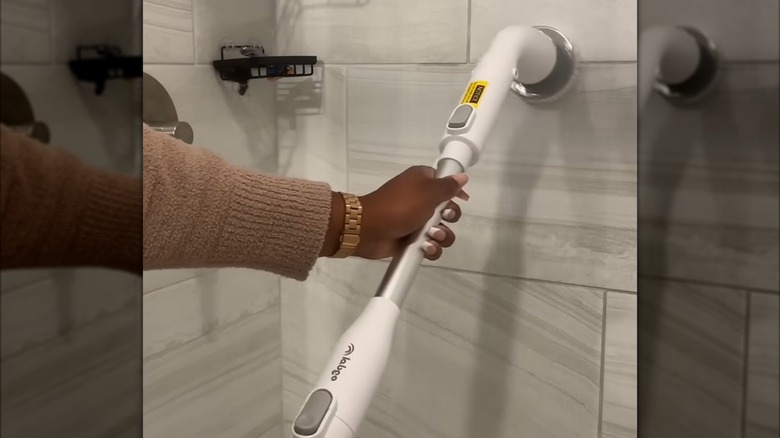 Person using a rotating long handle brush to clean shower