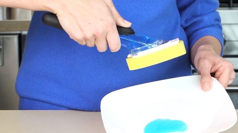 person holding soap dispensing sponge filled with blue dish soap above a plate