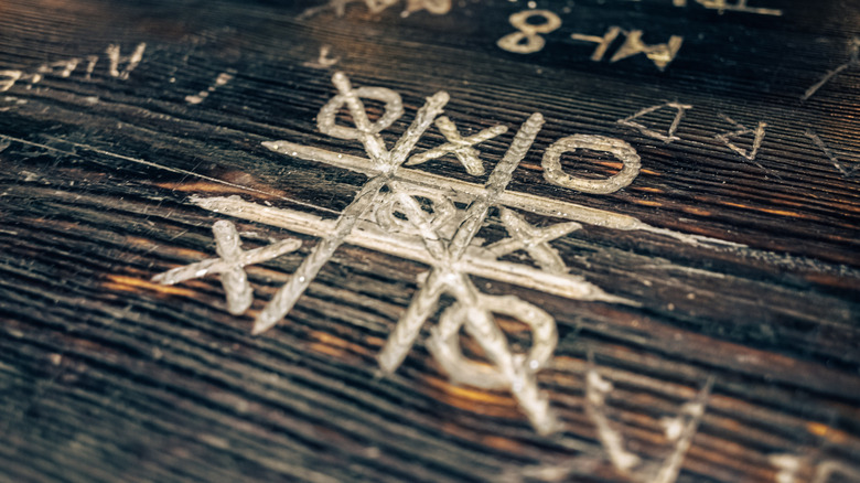 People play tic tac toe on a wooden board by carving into the wood.