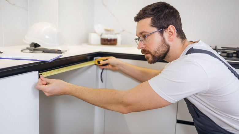 A person measures the width of a cabinet's opening using a tape measure