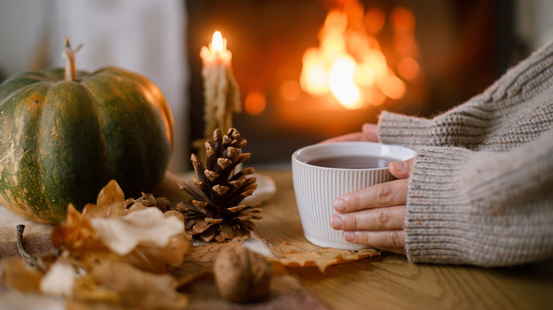 A person with a cup of tea with autumnal objects and a candle on the table