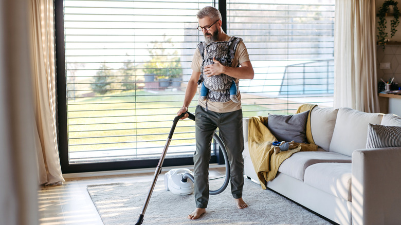 A man vacuuming an area rug in his living room