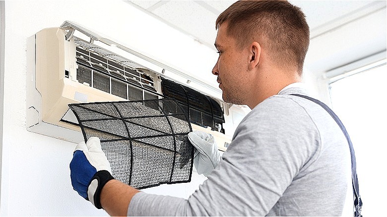 A professional wearing gloves holds an air-conditioner filter after removing it