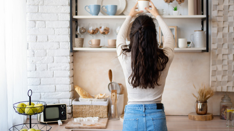 Person organizing kitchen items on open shelving