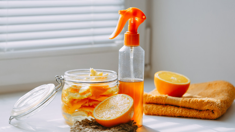 Fresh oranges and peels next to an orange cleaning solution in a spray bottle.