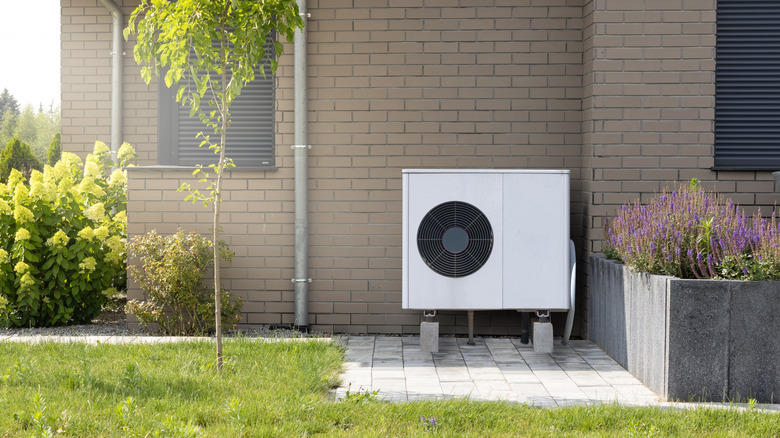 A boxy white heat pump has been installed on the outside of a brick building