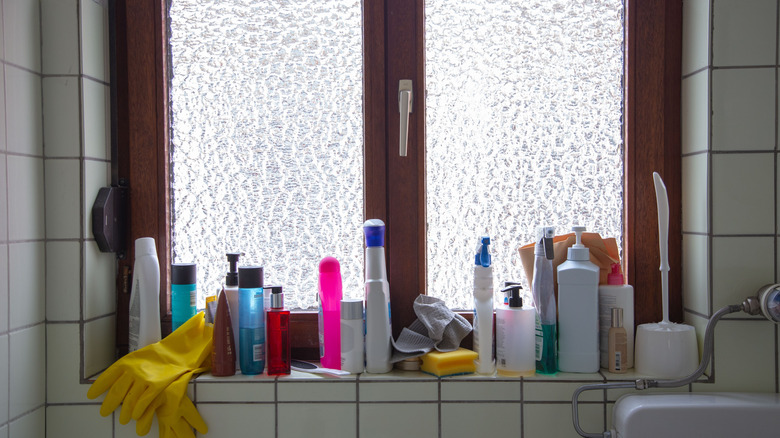 Cleaning supplies and skincare on a cluttered window sill