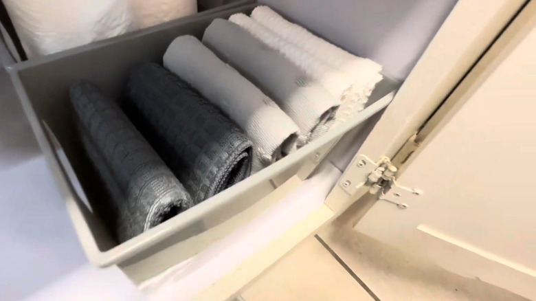 Gray bin with folded towels inside in cabinet