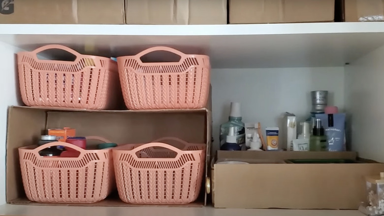 Four pink baskets sit inside and on top of a cardboard storage solution in a cabinet