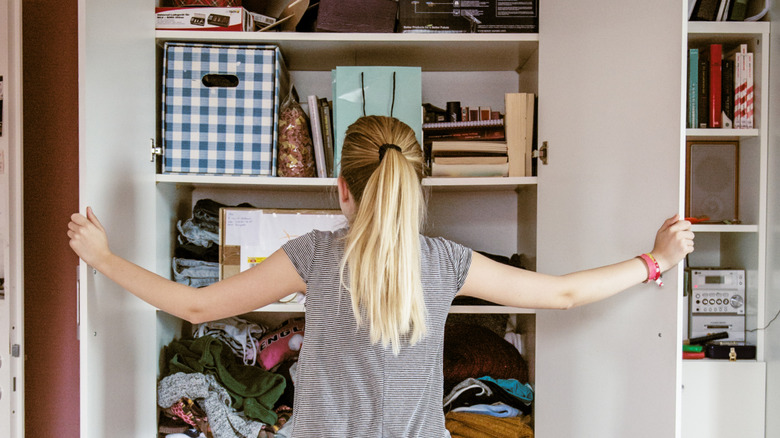 woman opening doors of disorganized closet