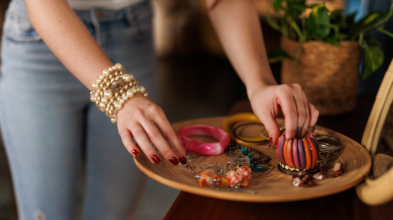 Woman choosing her jewelry from a messy tray on a table