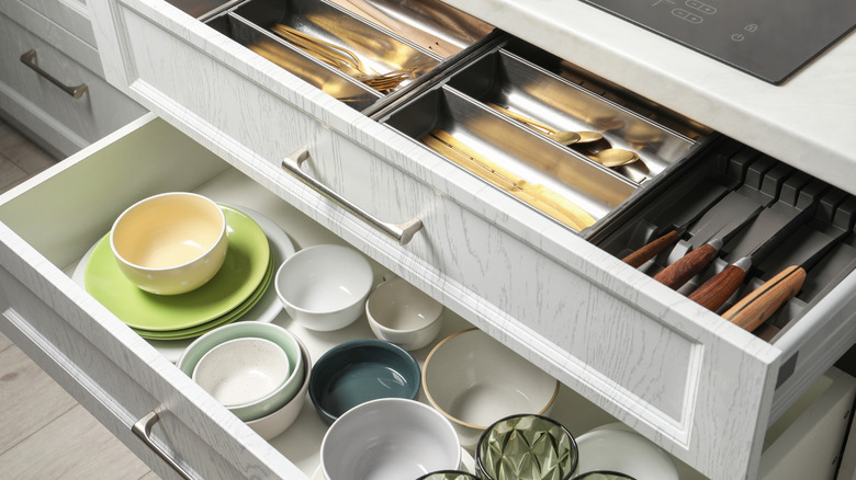 Two kitchen drawers open with bowls and plates in the bottom drawer and cutlery on top