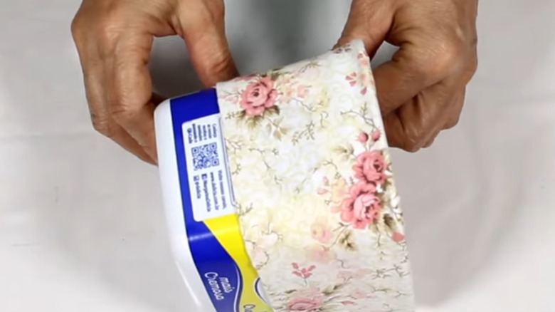 A person's hands line a plastic tub with floral fabric.