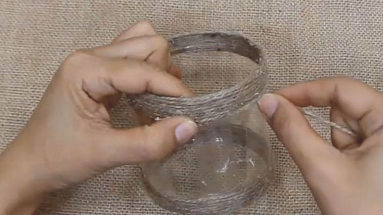 Person winding twine around a plastic tube to make toilet paper holder