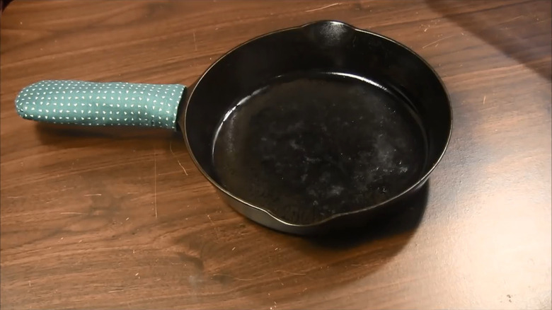 Green fabric sleeve made of a pot holder on handle of cast iron skillet