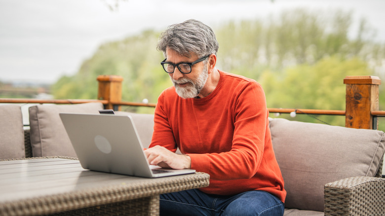 Man on a patio in an orange shirt looking at his laptop