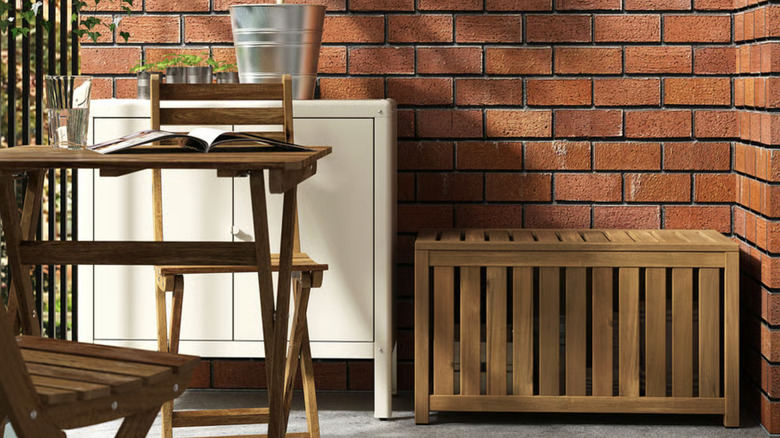 NÄMMARÖ storage box on a patio with a brick wall a patio table and chairs set.