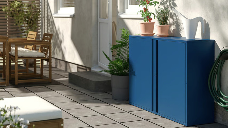 Blue SUNDSÖ cabinet on a bright patio with potted plants on top of it.