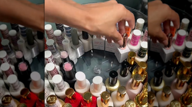 A person takes a bottle of nail polish fro a lazy Susan filled with more bottles.