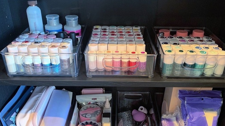 Acrylic bins filled with nail polish bottles and nail supplies organized on shelves in a cupboard.